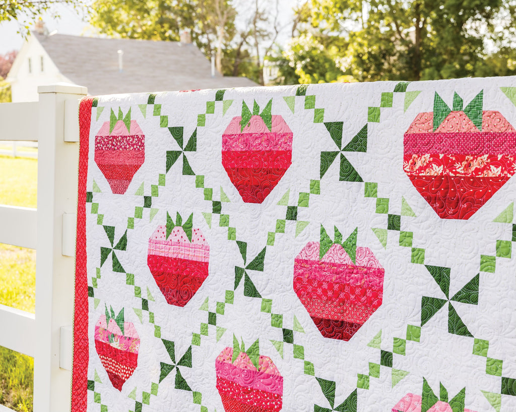 Quilt with pink and red strawberries hanging on a fence 