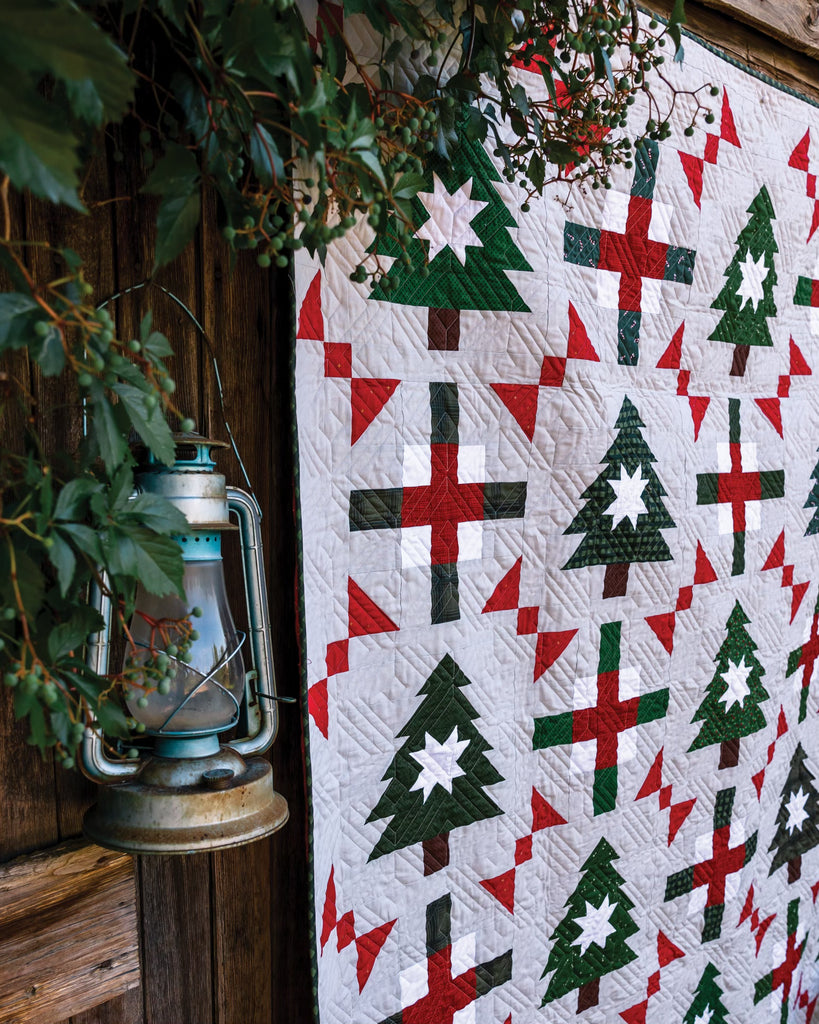 Hanging quilt with green pine trees and other red and green designs on a white base 