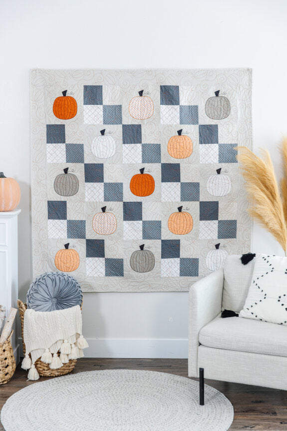 One Hoop Wonder Pumpkin patch Quilt hanging on a wall behind a chair and basket 