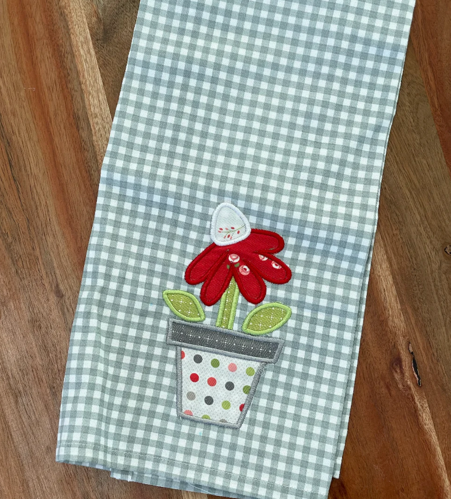 A tea towel with an embroidered applique flower in a pot. 